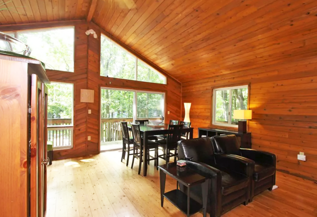 Rustic wood paneled den of cottage featuring large windows overlooking the woods